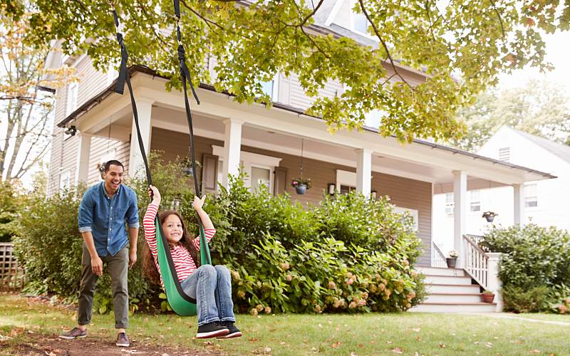 a father and daughter playing on the swing outside their home