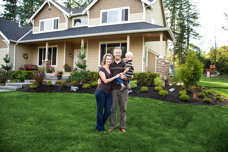 family of three standing outsite their home with trees surrounded