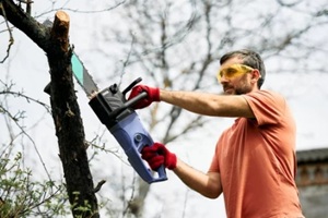 man cutting trees using electrical chainsaw in motion at his backyard
